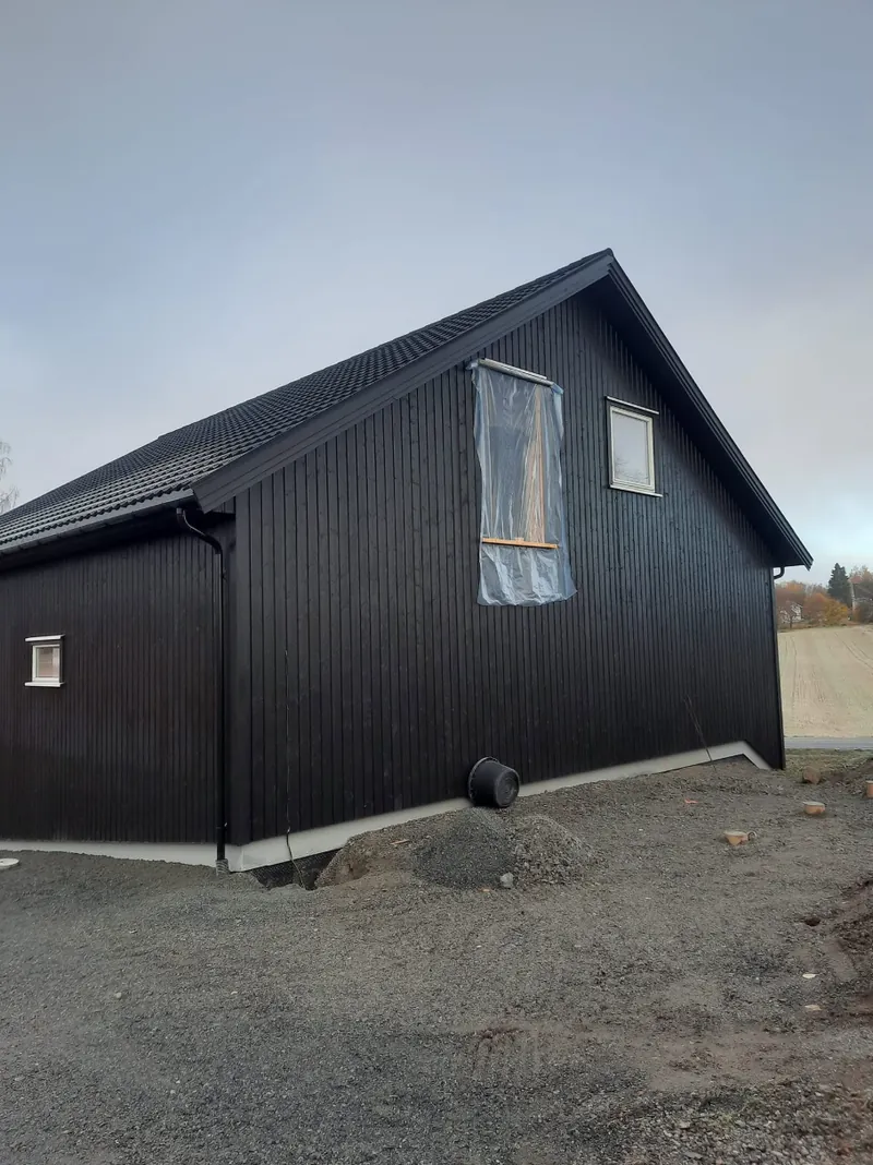 Garasjen sett fra siden, med sort kledning og vinduer i gavlen