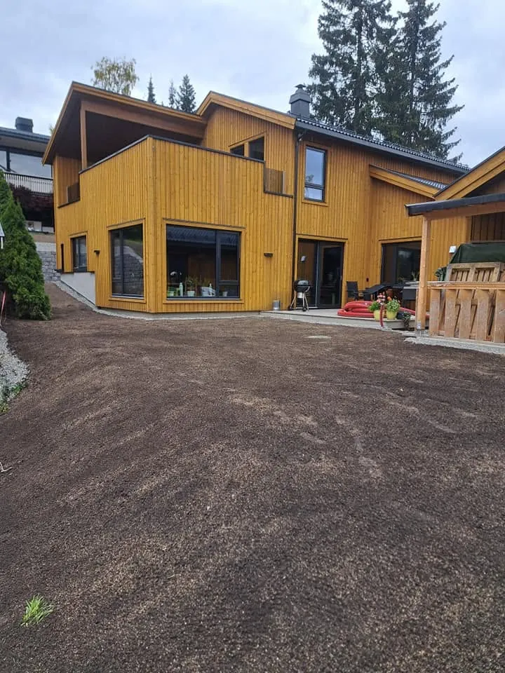 Gult hus med nyplanert uteområde med matjord, klart for plen